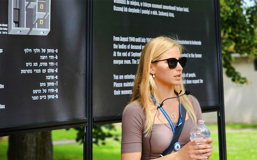 Guide explaining Auschwitz Birkenau history during a tour, standing near informational boards.