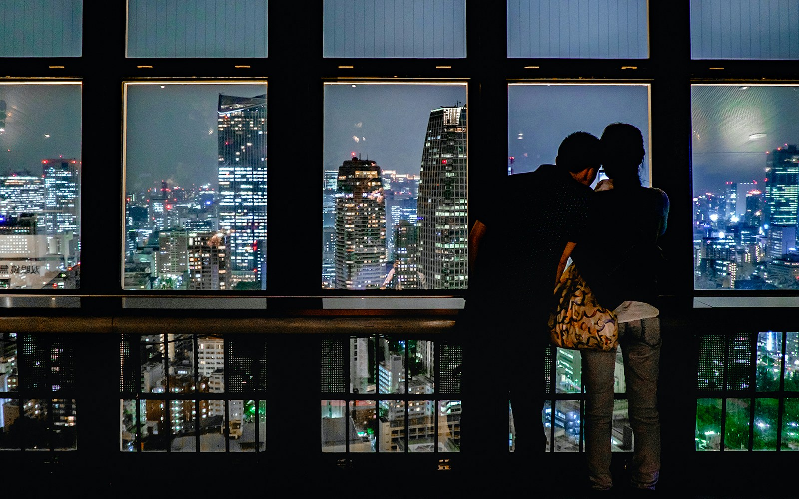 Couple enjoying Tokyo cityscape at night from Tokyo Tower observation deck.