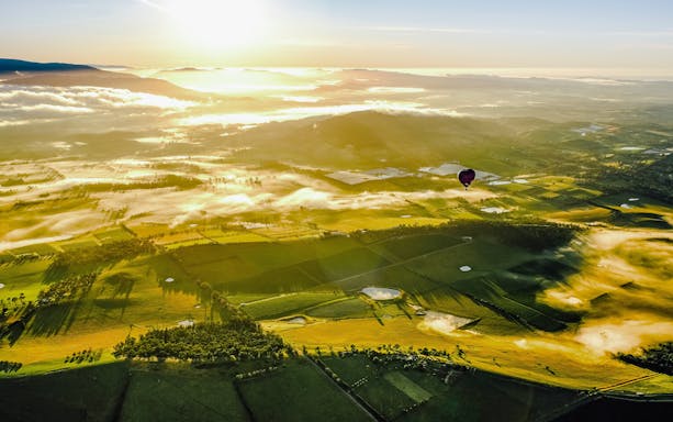 Hot air balloon over Yaara Valley at sunrise, with misty fields and distant hills.