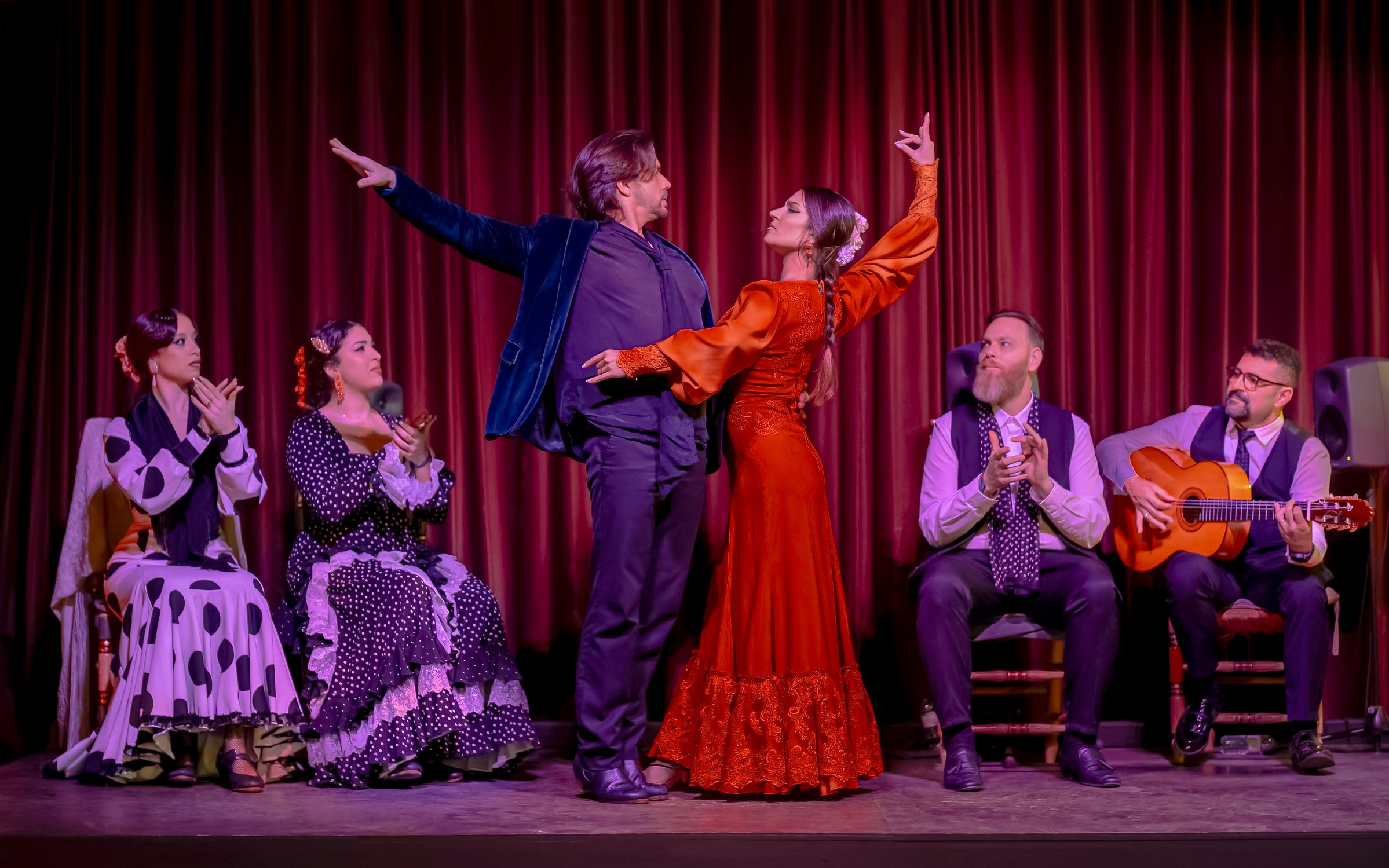 Flamenco dancers performing at Palau Dalmases with musicians and audience clapping.