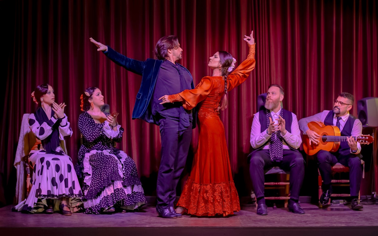 Flamenco dancers performing at Palau Dalmases with musicians and audience clapping.