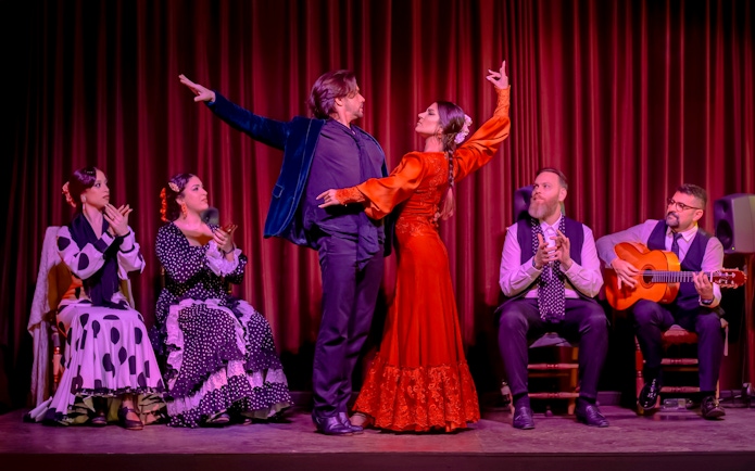 Flamenco dancers performing at Palau Dalmases with musicians and audience clapping.