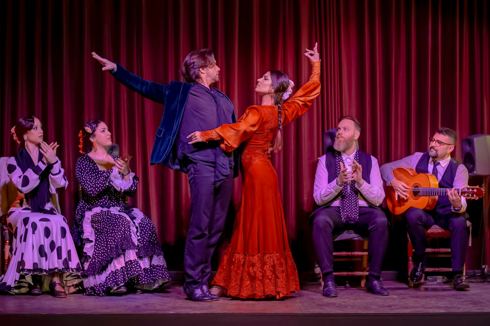 Flamenco dancers performing at Palau Dalmases with musicians and audience clapping.