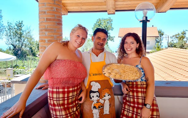 Neapolitan chef with guests holding pasta during Amalfi Coast cooking class.
