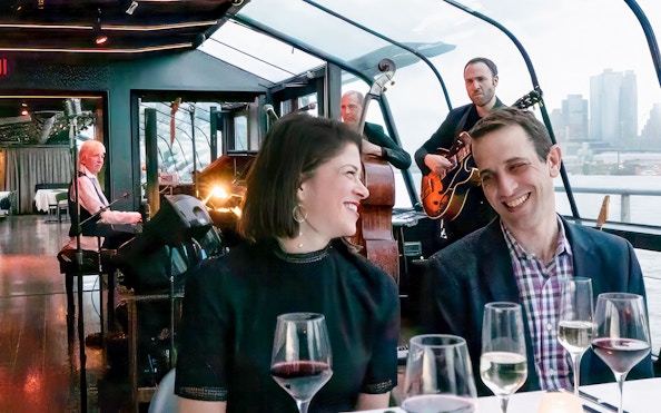 Couple dining with live jazz band on a river cruise with city skyline view.