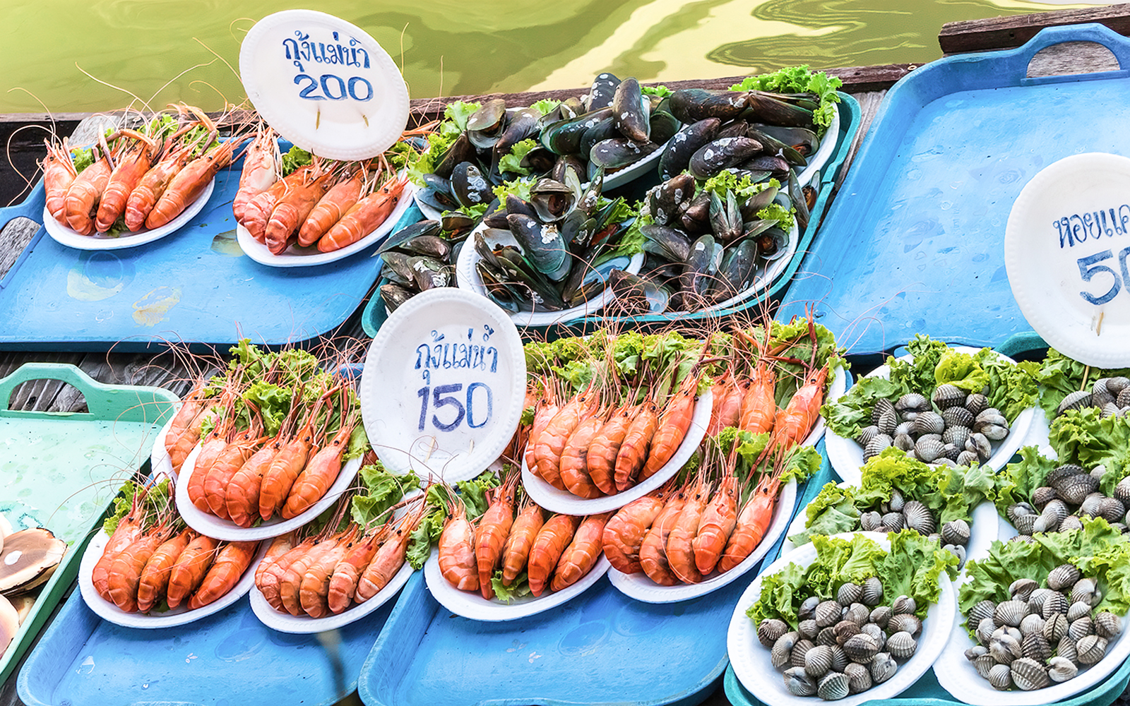 Barbecued seafood displayed on trays at Amphawa floating market in Thailand.