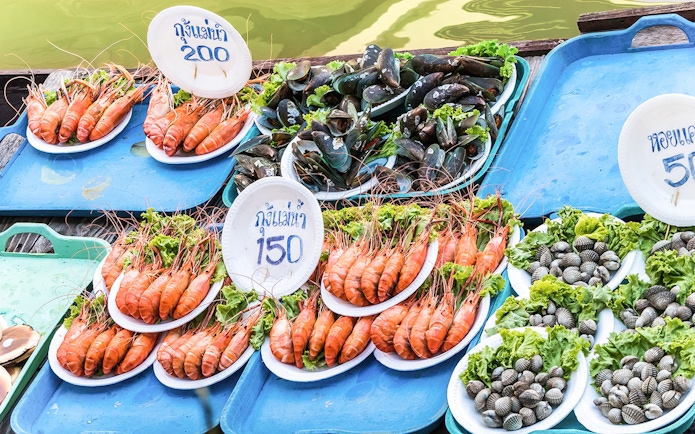 Barbecued seafood displayed on trays at Amphawa floating market in Thailand.