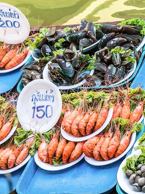 Barbecued seafood displayed on trays at Amphawa floating market in Thailand.