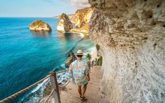 Tourist descending steps with view of Atuh Cliff and ocean on Nusa Penida Island.