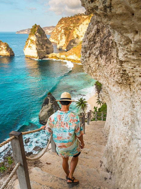 Tourist descending steps with view of Atuh Cliff and ocean on Nusa Penida Island.