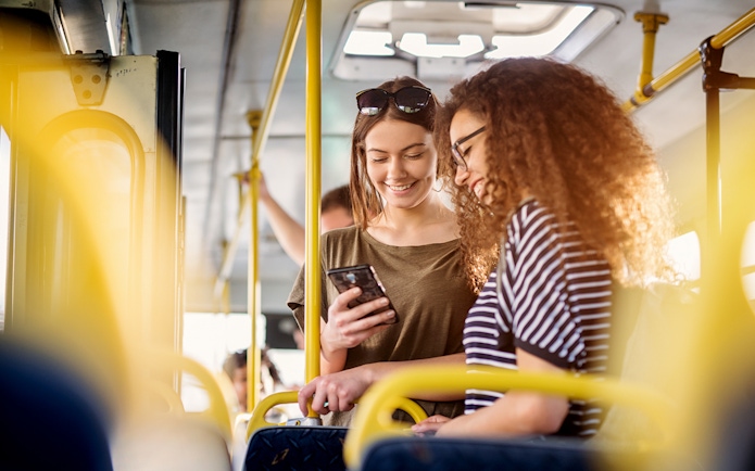 Two women smiling and looking at a phone on a bus.