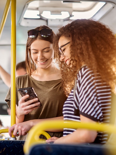 Two women smiling and looking at a phone on a bus.