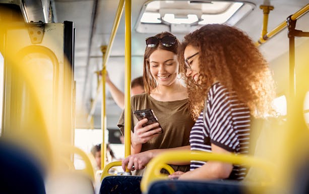Two women smiling and looking at a phone on a bus.