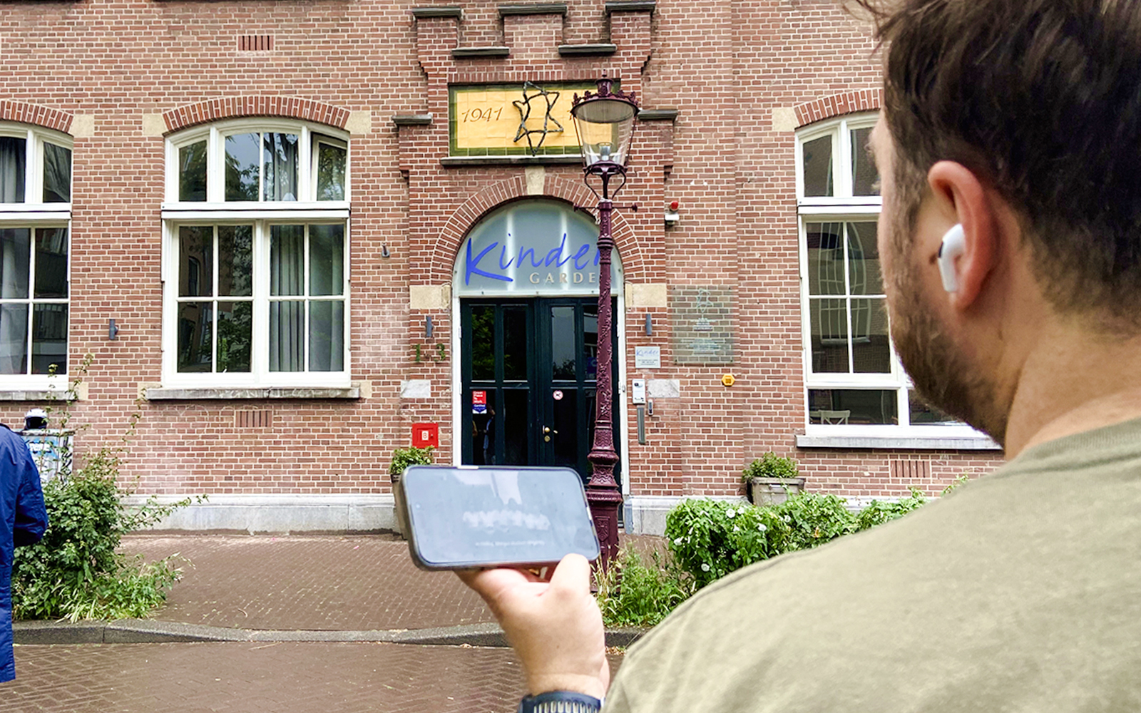 Guest using mobile guide outside Kinder Garden building on Anne Frank tour, Amsterdam.