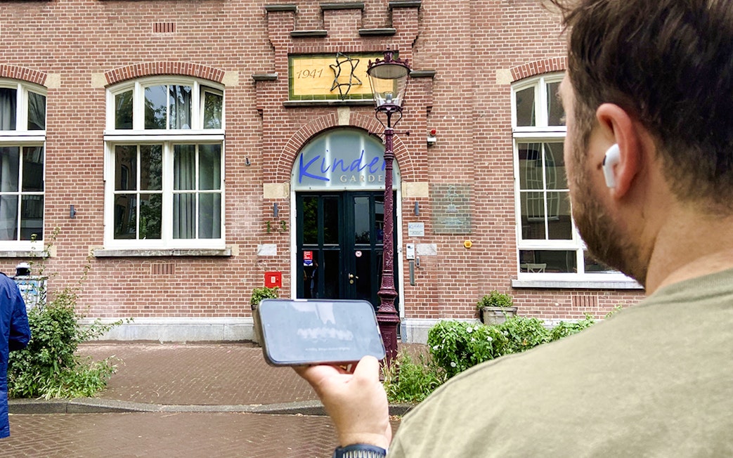 Guest using mobile guide outside Kinder Garden building on Anne Frank tour, Amsterdam.