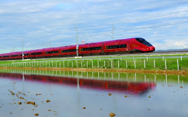 High-speed red train traveling through Italian countryside between Milan and Venice.