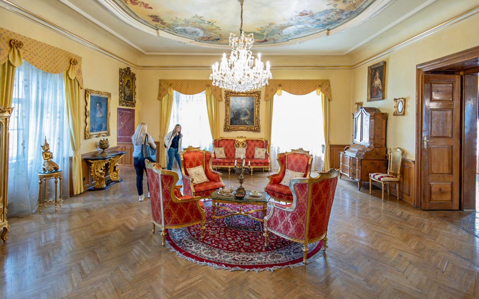Living room with ornate red furniture and chandelier in Baroque castle, Prague.
