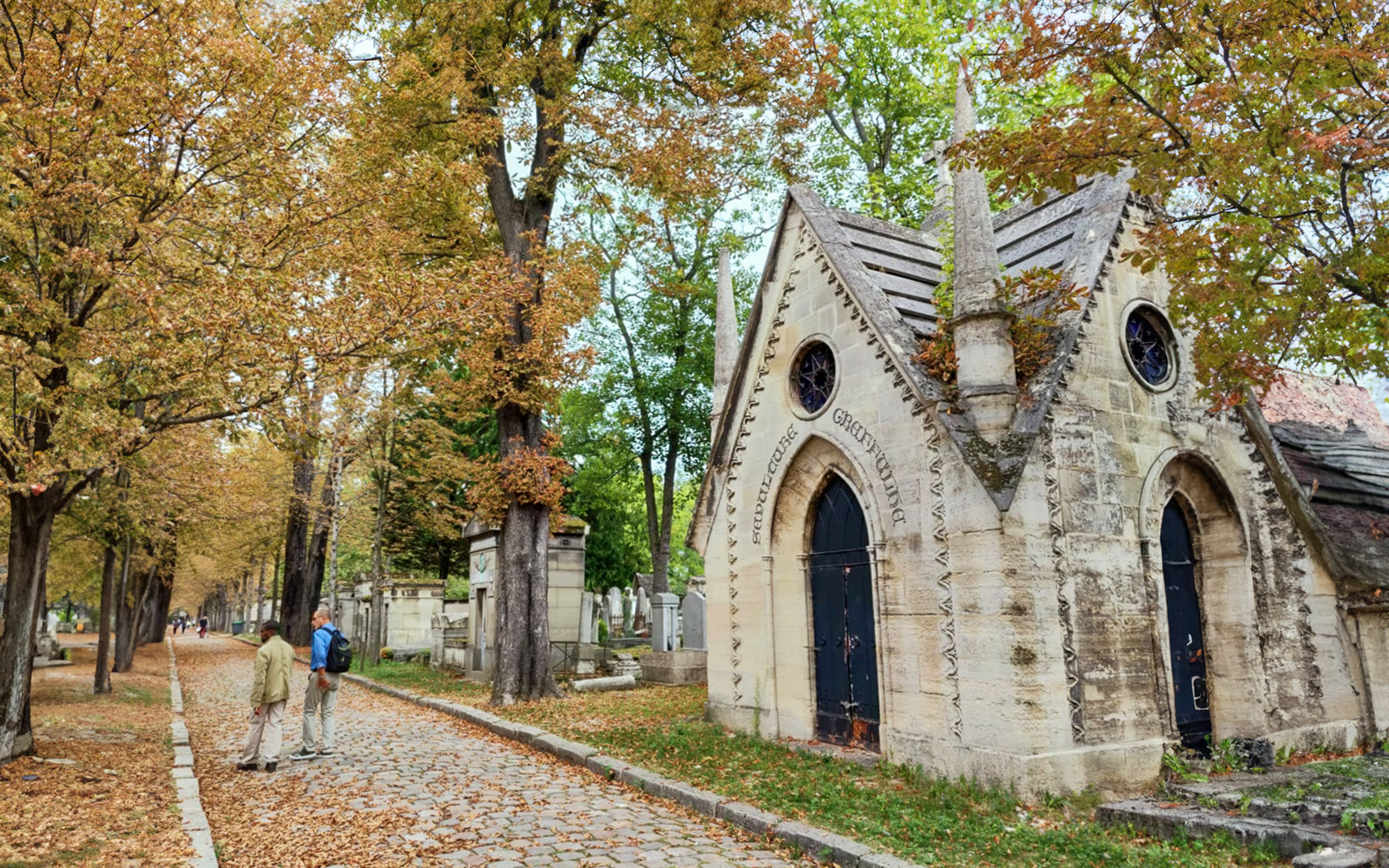 Père-Lachaise Cemetery path with mausoleum and visitors in Paris.
