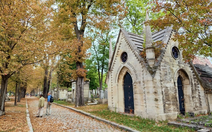 Père-Lachaise Cemetery path with mausoleum and visitors in Paris.