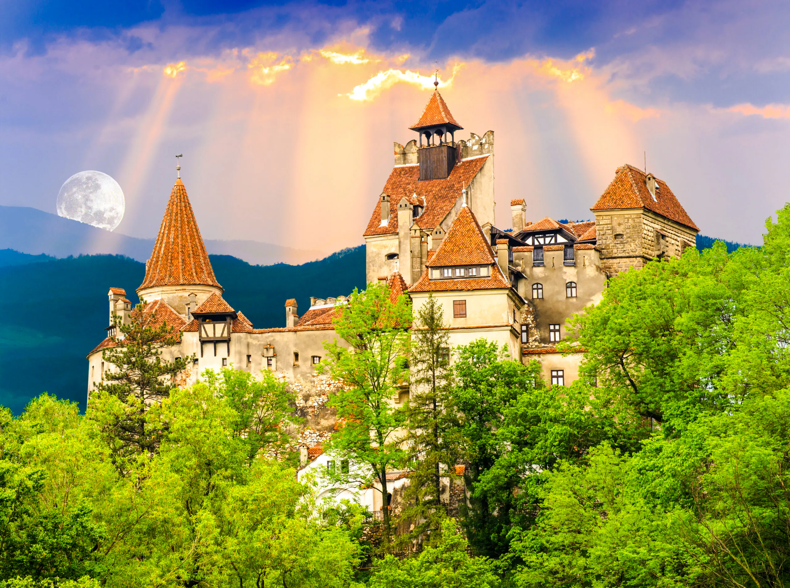 Brasov's Bran Castle surrounded by lush greenery under a full moon.