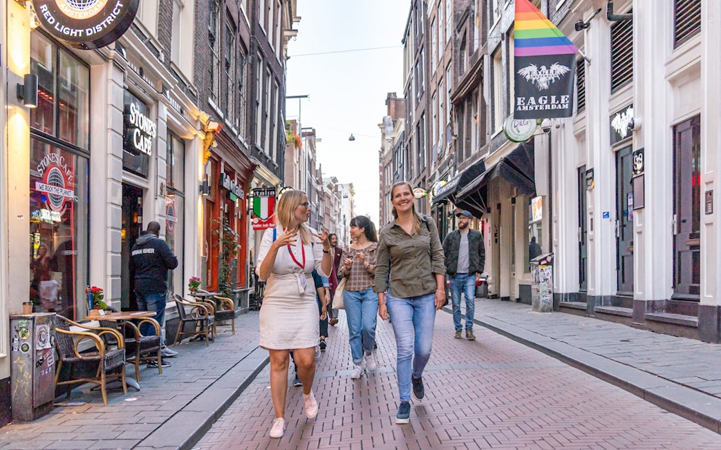 Tour group walking through Amsterdam's Red Light District with guide, near coffeeshops.