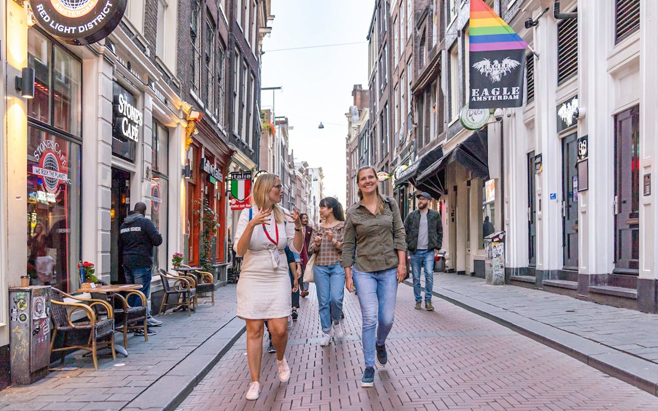 Tour group walking through Amsterdam's Red Light District with guide, near coffeeshops.