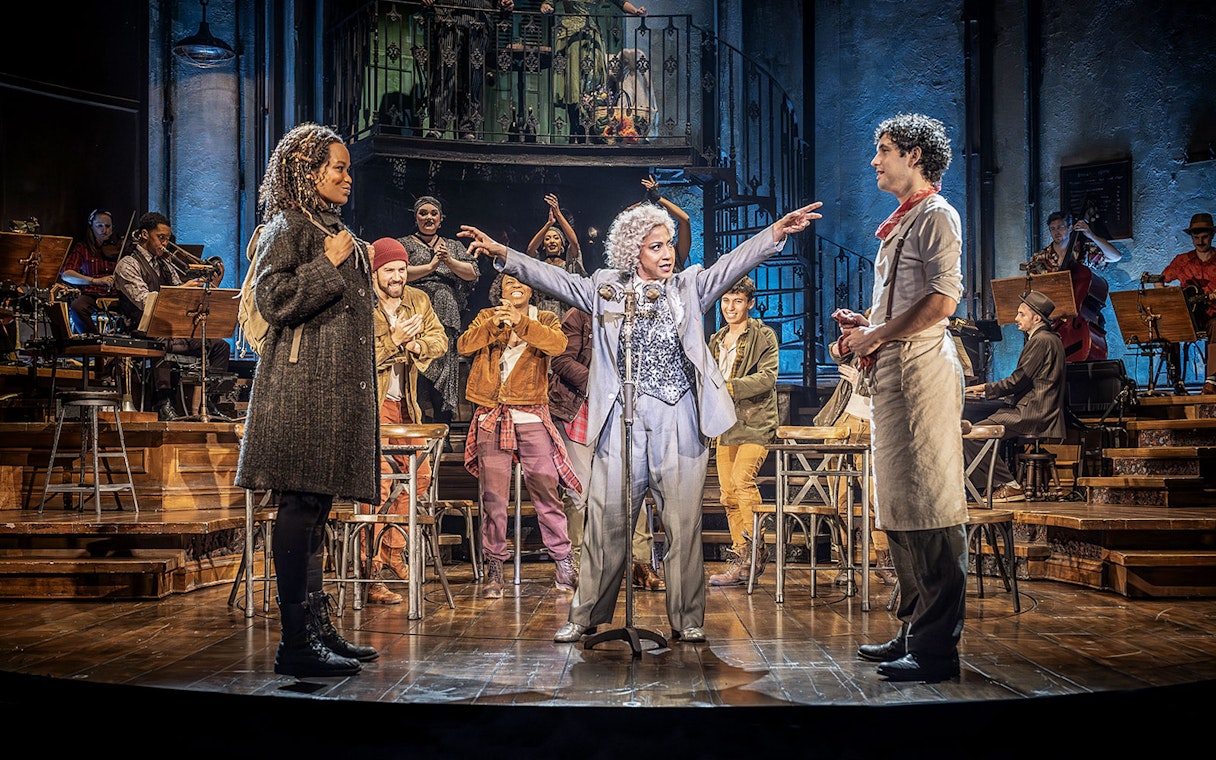 Stage performance of Hadestown with actors and musicians in a lively scene.