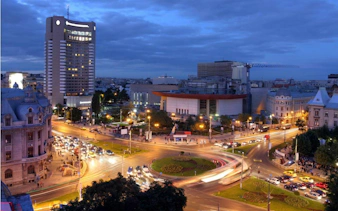Bucharest cityscape at dusk with illuminated streets and modern buildings.