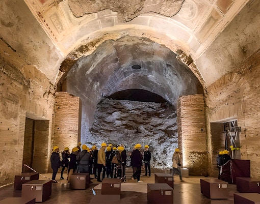 Visitors with helmets exploring Domus Aurea's ancient ruins in Rome.