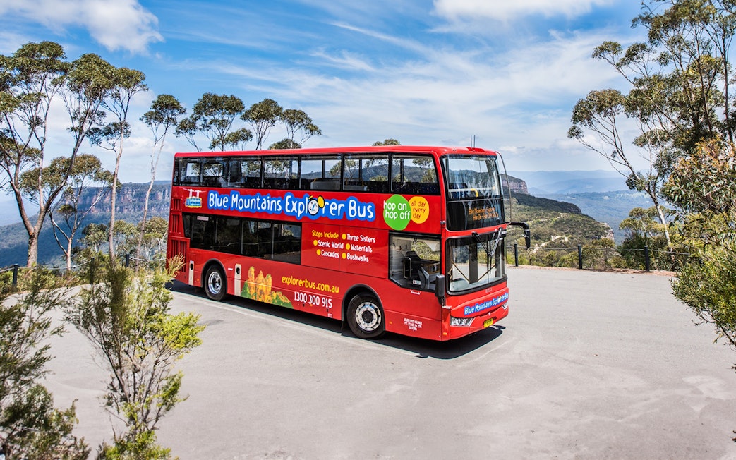 Red double-decker bus on Blue Mountains Hop-On Hop-Off Tour with scenic view.