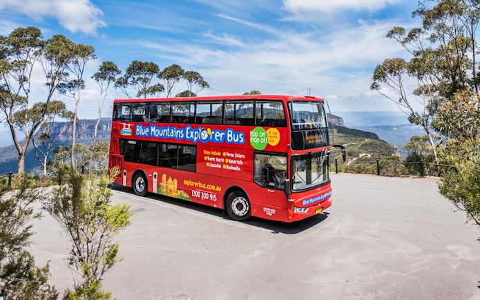 Red double-decker bus on Blue Mountains Hop-On Hop-Off Tour with scenic view.
