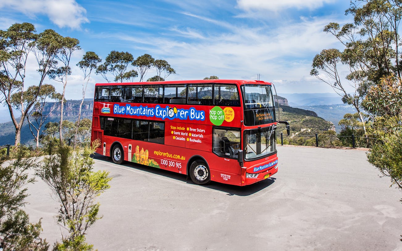 Red double-decker bus on Blue Mountains Hop-On Hop-Off Tour with scenic view.