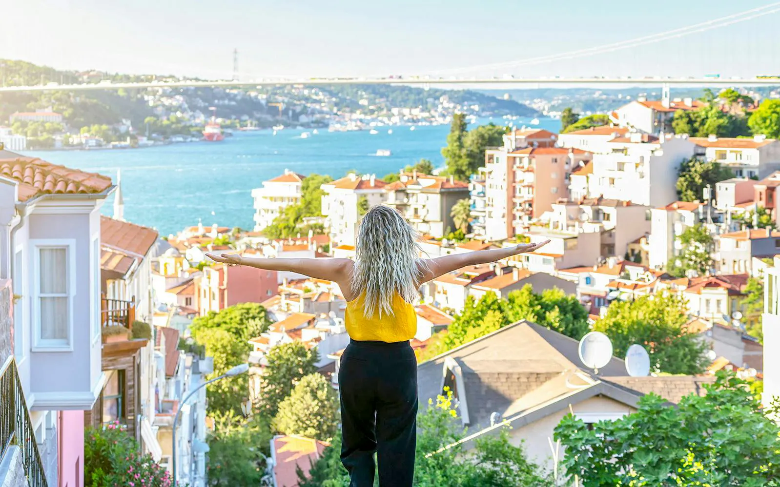 Person overlooking Istanbul rooftops with Bosphorus Bridge in the background.