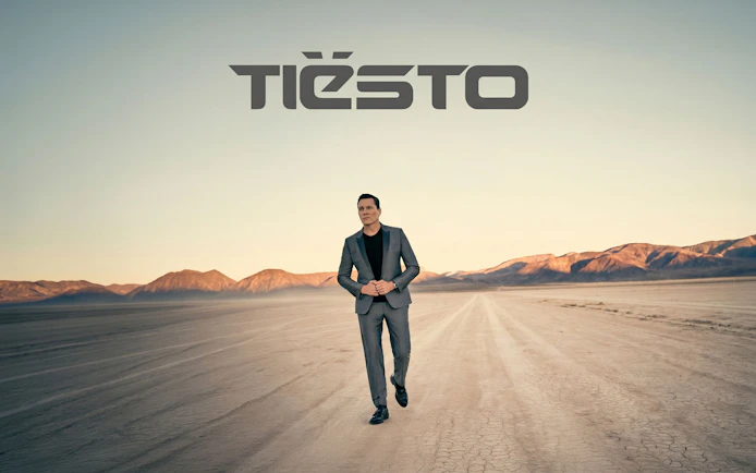 Tiësto walking on a desert landscape with mountains in the background, Ibiza tour promotion.