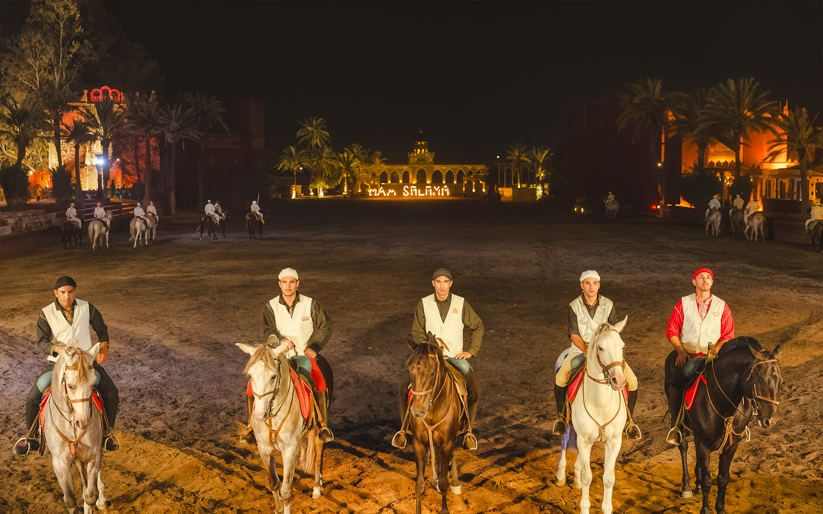 Horsemen at Chez Ali Dinner & Fantasia Show in Marrakech, Morocco, with illuminated backdrop.