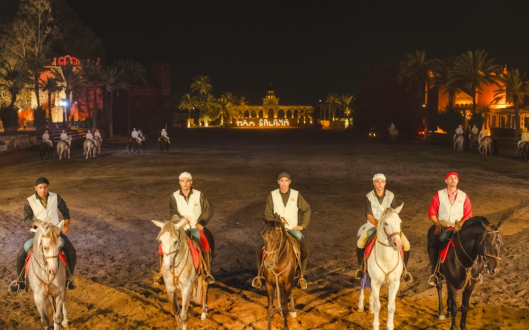 Horsemen at Chez Ali Dinner & Fantasia Show in Marrakech, Morocco, with illuminated backdrop.