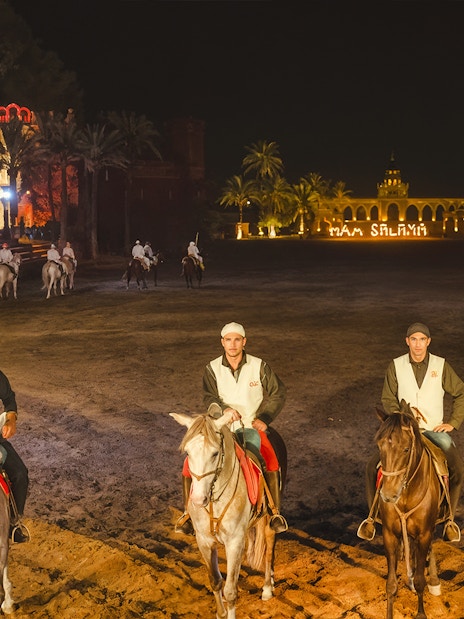 Horsemen at Chez Ali Dinner & Fantasia Show in Marrakech, Morocco, with illuminated backdrop.