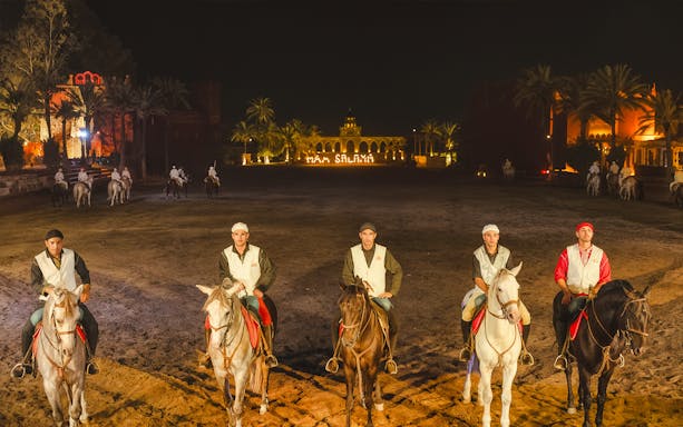 Horsemen at Chez Ali Dinner & Fantasia Show in Marrakech, Morocco, with illuminated backdrop.