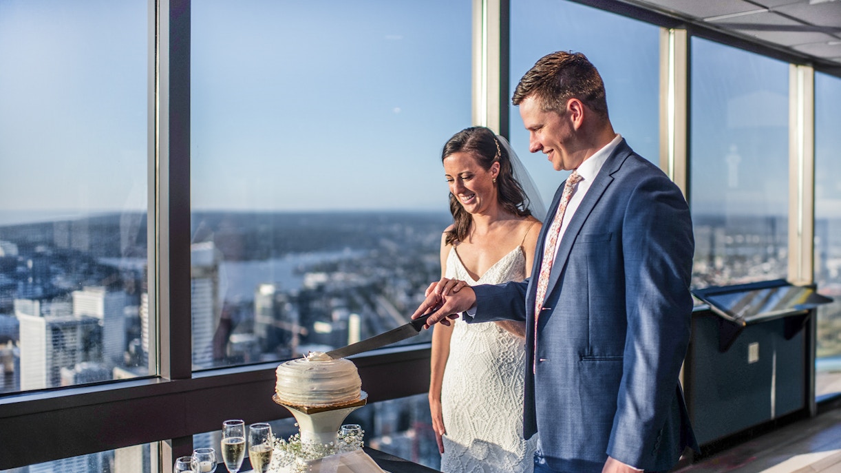 Couple cutting cake at Sky View Observatory with cityscape view.