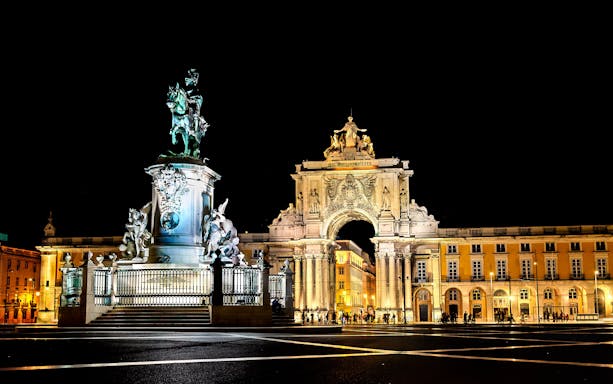 Commerce Square in Lisbon, Portugal illuminated at night with equestrian statue and arch.