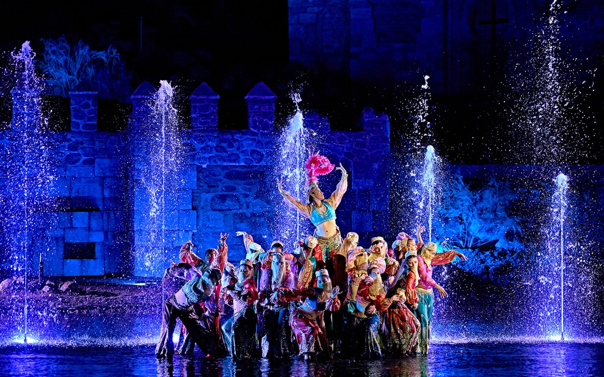 Performers in colorful costumes at a night show with fountains at Puy du Fou España.