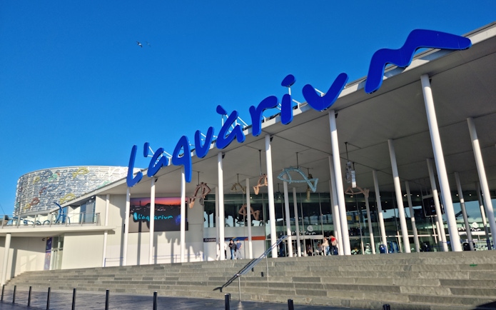 Entrance of L'Aquàrium de Barcelona with blue signage and modern architecture.