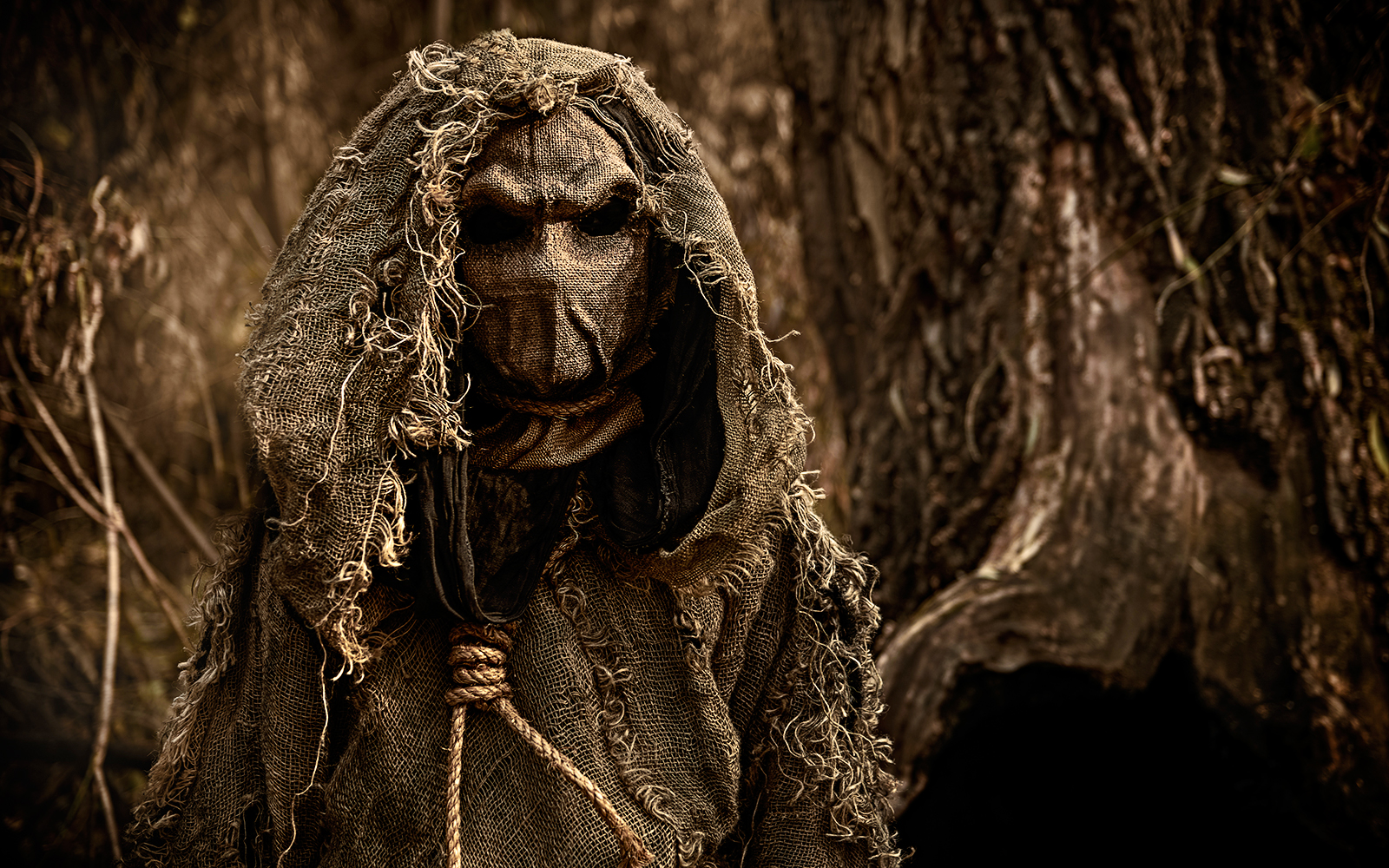 Scarecrow figure in burlap hood at horror house attraction.