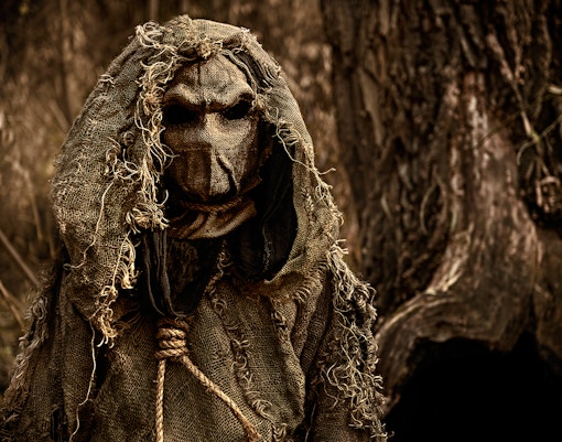 Scarecrow figure in burlap hood at horror house attraction.