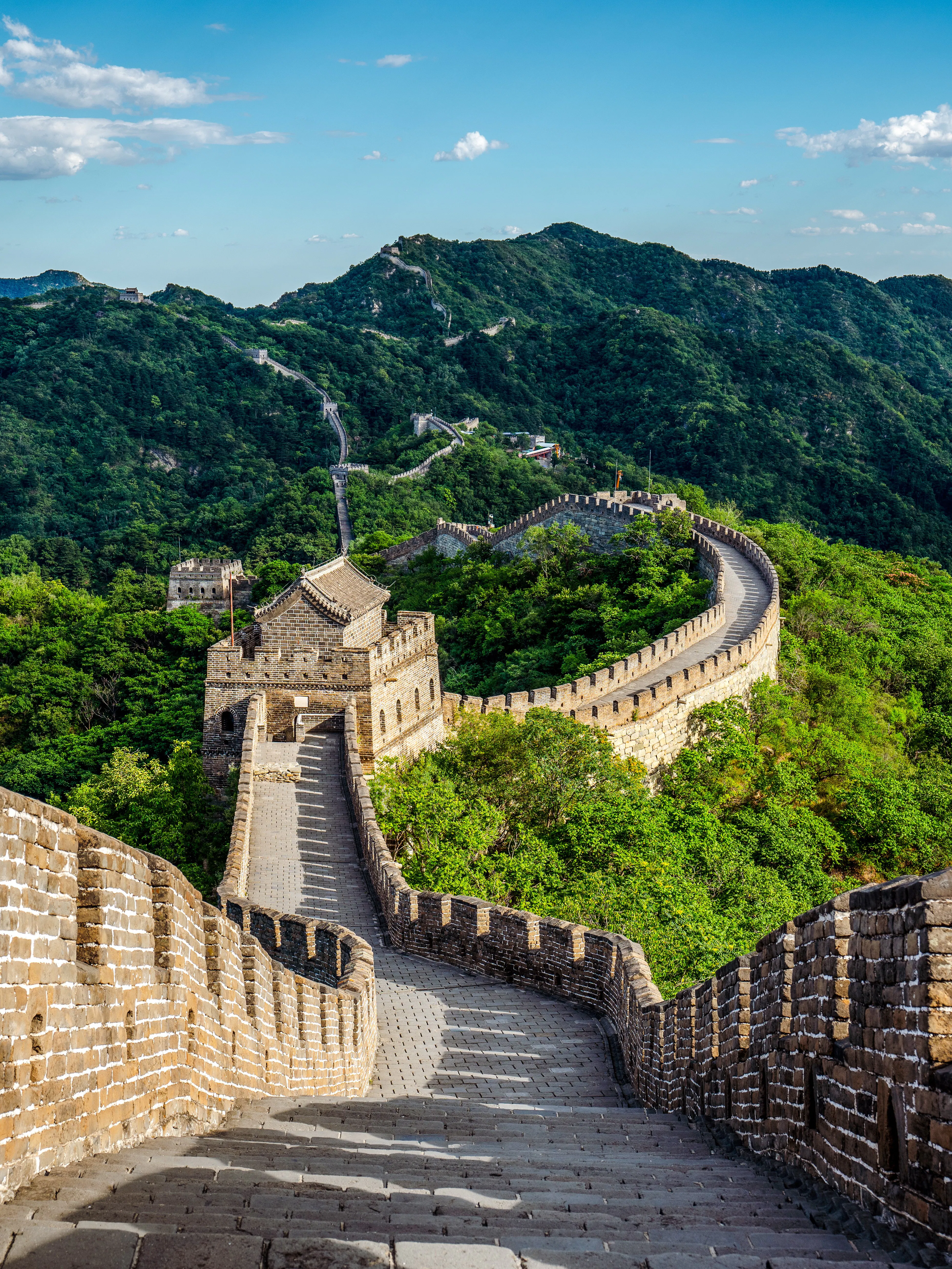 Great Wall of China winding through lush green mountains under a clear blue sky.