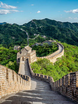Great Wall of China winding through lush green mountains under a clear blue sky.