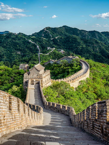 Great Wall of China winding through lush green mountains under a clear blue sky.