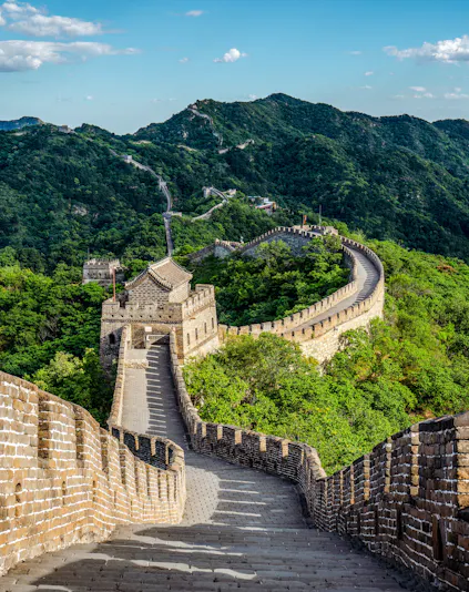 Great Wall of China winding through lush green mountains under a clear blue sky.