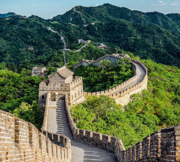 Great Wall of China winding through lush green mountains under a clear blue sky.