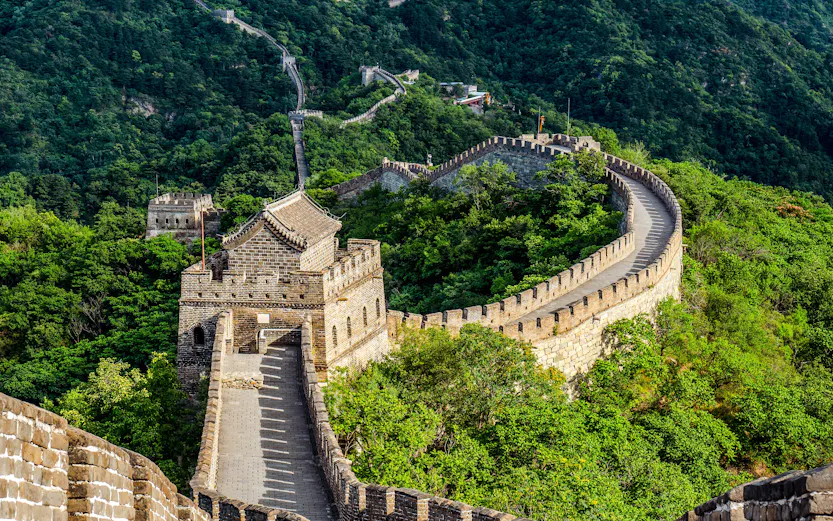 Great Wall of China winding through lush green mountains under a clear blue sky.